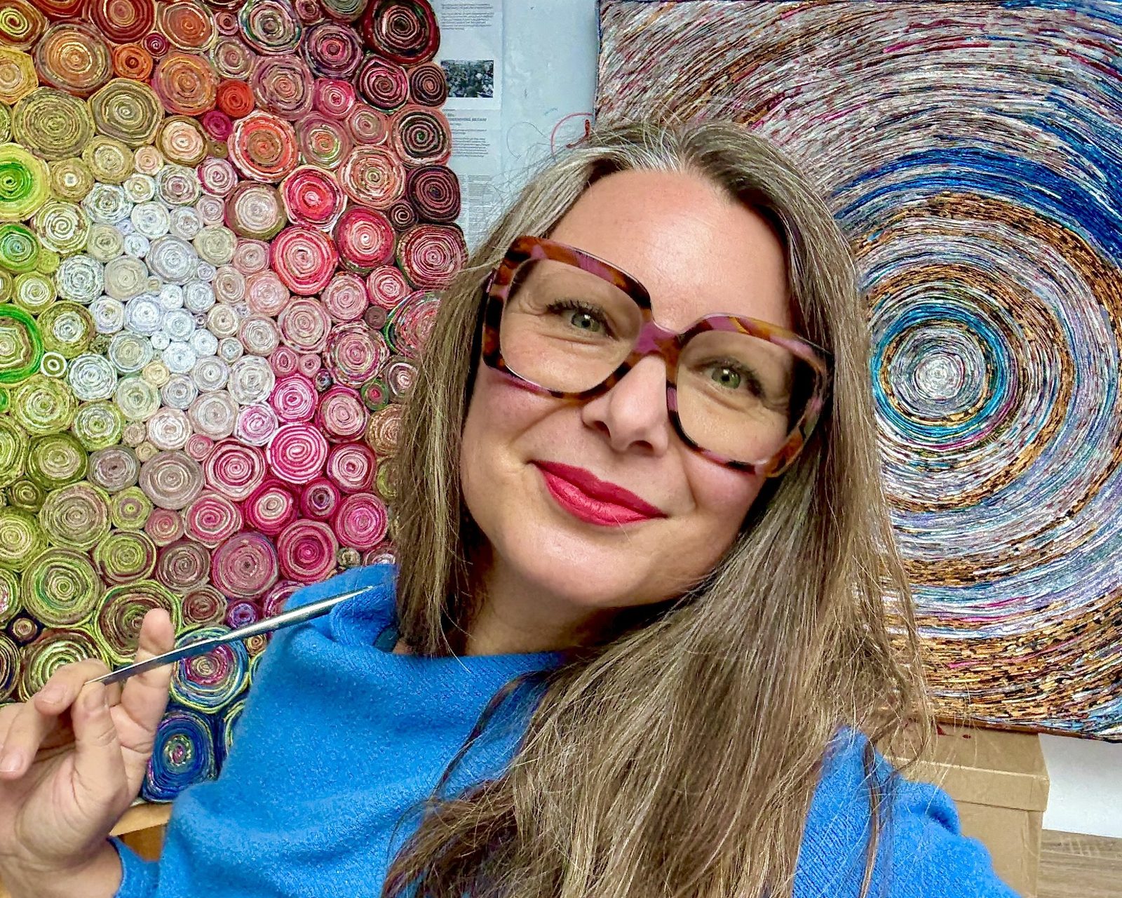Francesca Busca in her studio in front of a large circular mosaic made from bottle tops.